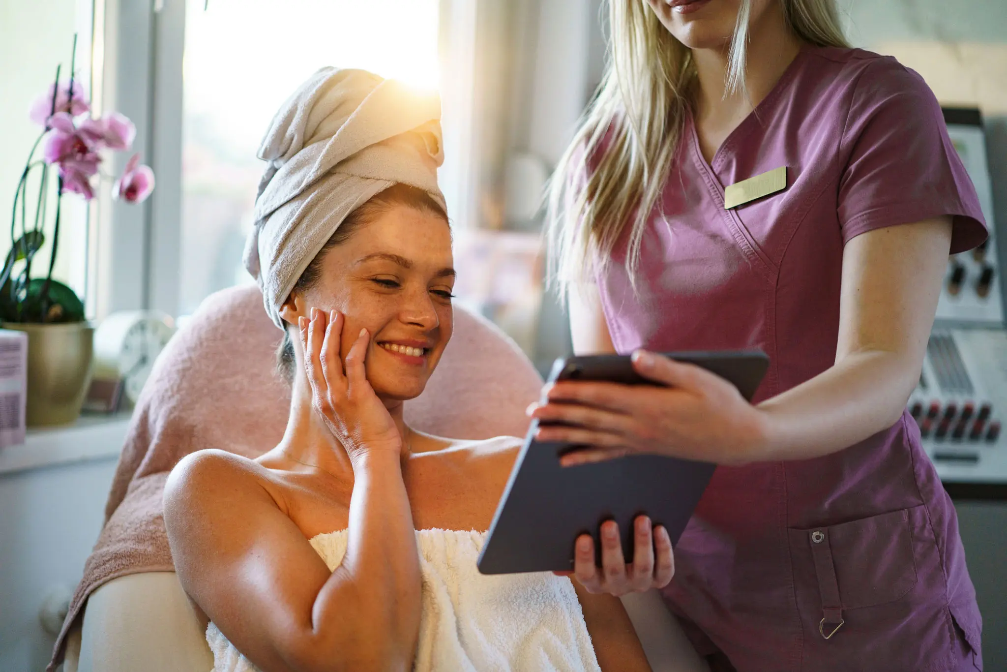 Woman at spa, viewing tablet with beautician.